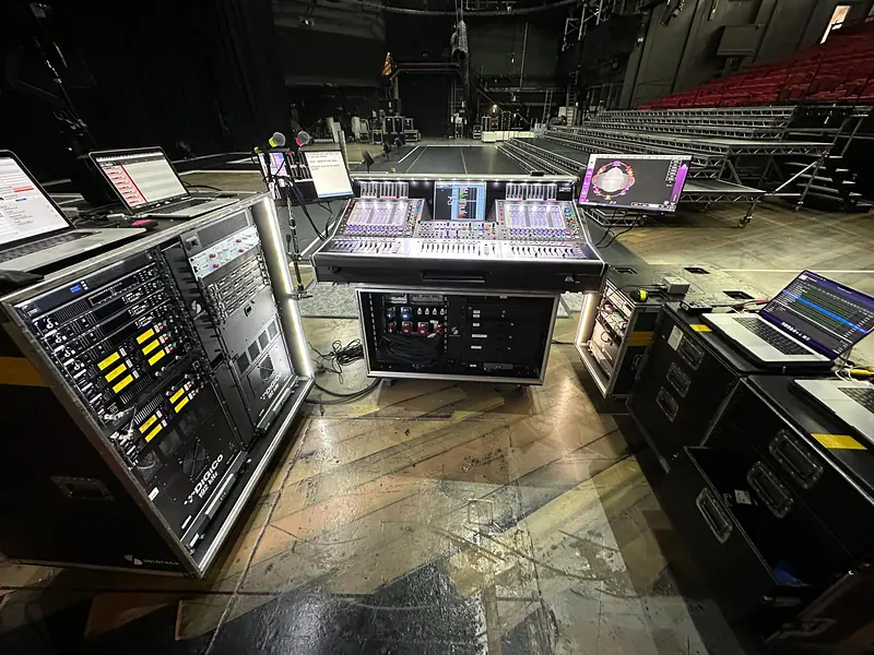 A DiGiCo console, racks and laptops set up on flight cases in an empty arena before the show